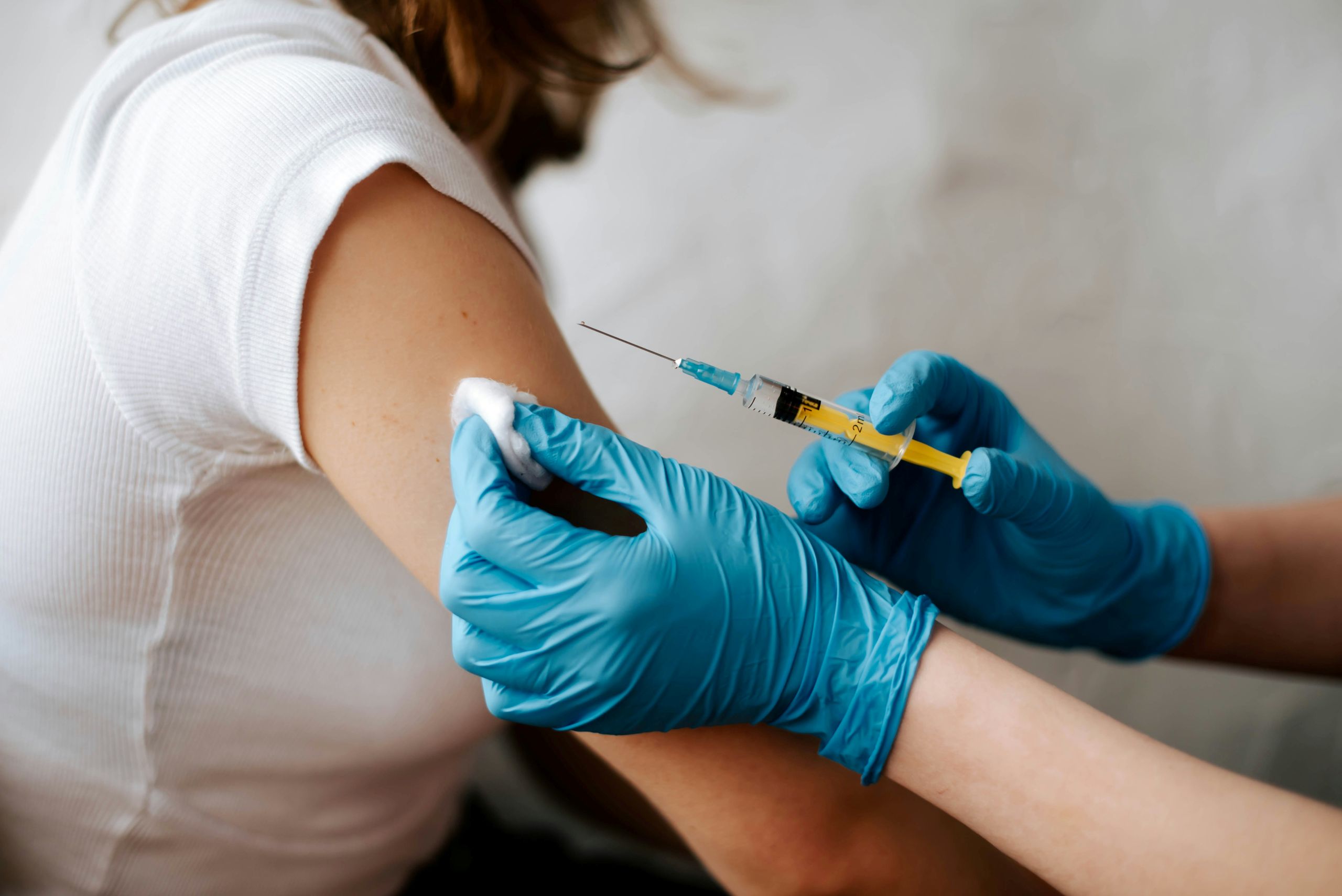 A healthcare worker wearing blue gloves prepares to give an injection in a patients upper arm.